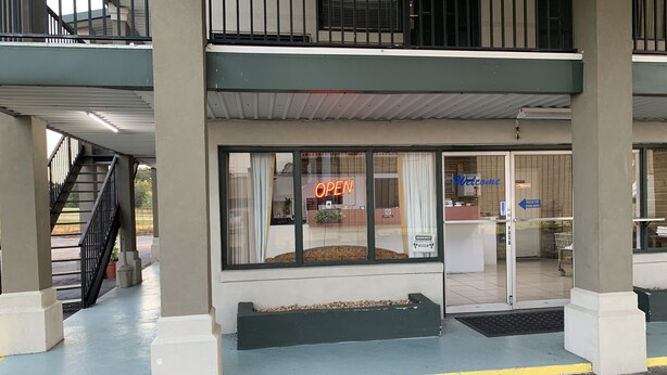 L’entrée d’un hôtel, avec un comptoir d’accueil, un panneau néon indiquant « OUVERT » et une pancarte « Bienvenue ».
