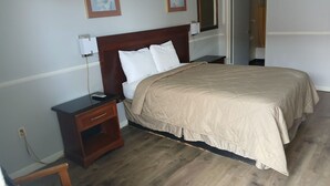 A neatly arranged bedroom with a large bed, bedside tables, a nightstand, and a chair. - Travelers Inn (Valdosta)
