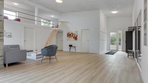 Un salón amplio con suelo de madera, un sofá gris, una silla moderna, una escalera y una puerta que da a un balcón.
