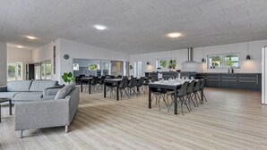 Un comedor espacioso y moderno con una larga mesa y sillas, un sofá y una zona de cocina con un ventanal grande.