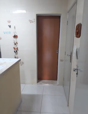 Une entrée de cuisine avec une porte marron, des murs recouverts de carreaux blancs et un sol carrelé.