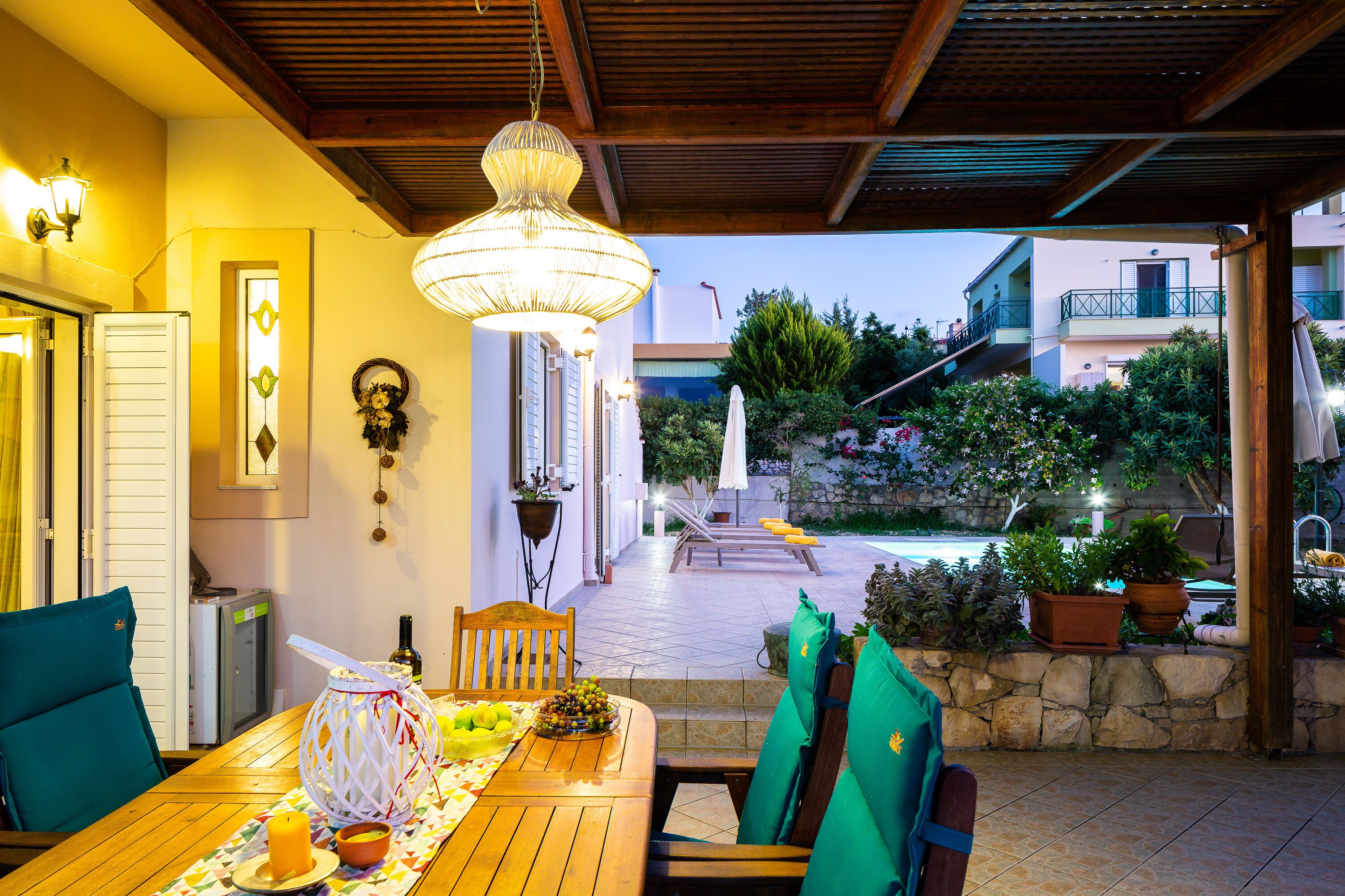 An outdoor dining area with a wooden table, chairs, and a hanging light fixture.