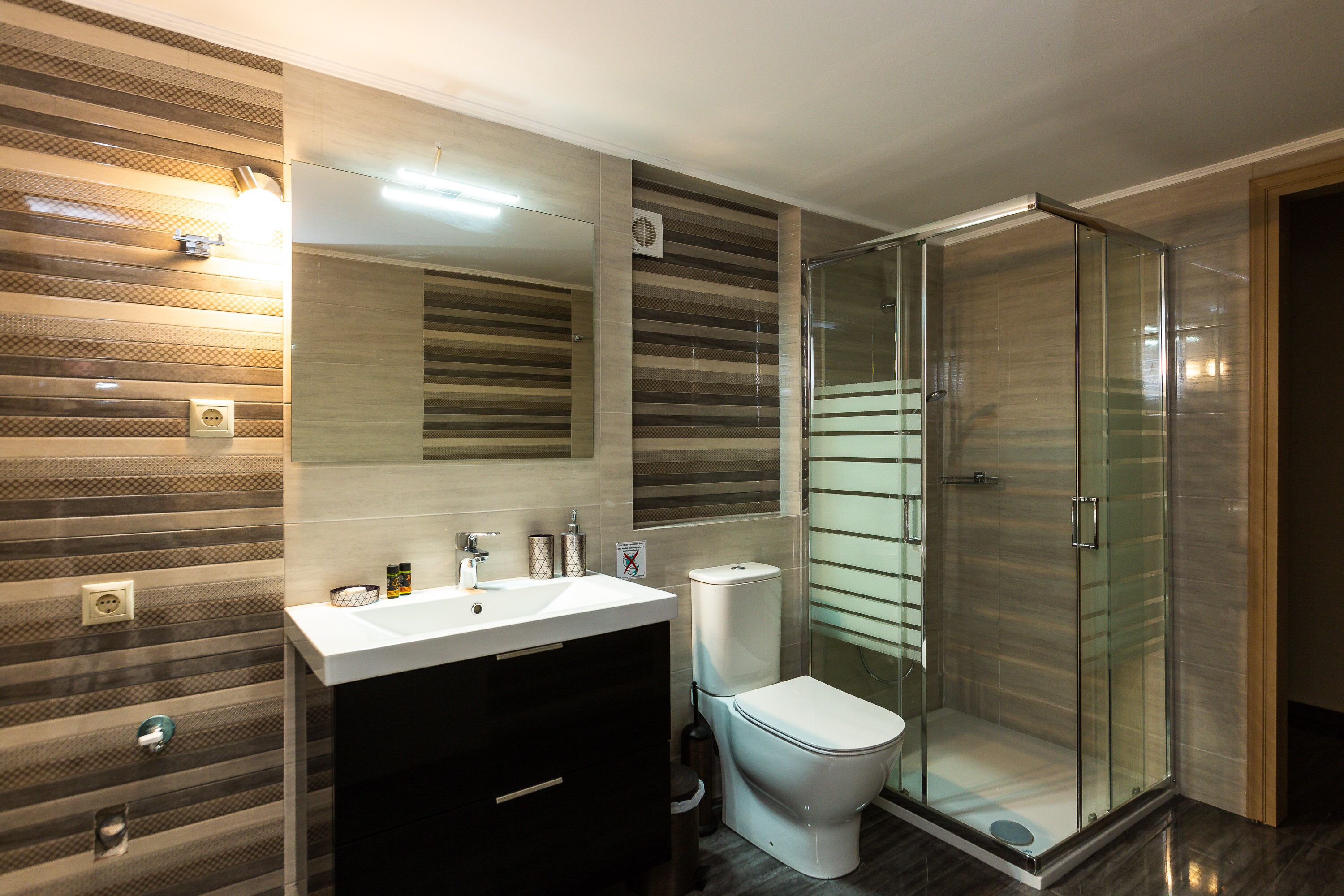 A modern bathroom with a glass-enclosed shower, a white sink, and a toilet.