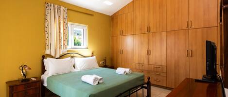 A bedroom with a bed, wooden wardrobe, and a desk with a television.