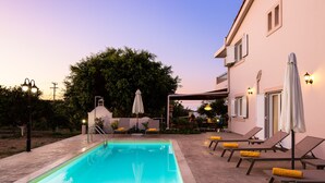 A swimming pool with lounge chairs and umbrellas, surrounded by a building with outdoor seating and a tree. - Villa Carpe Diem -Luxury Villa with private pool     2 km from the beach! (Adele)