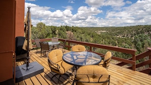 A wooden deck with a table and chairs, overlooking a forested landscape.