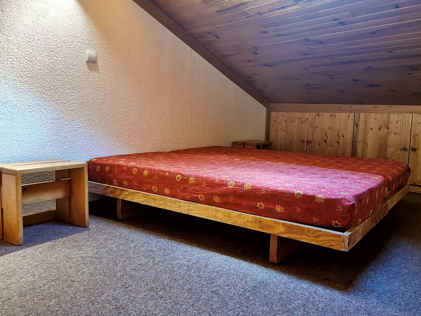 Quarto pequeno com uma cama de solteiro, teto inclinado, paredes de madeira e chão coberto por carpete.