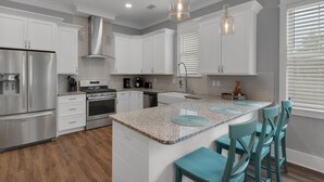 A modern kitchen with white cabinets, stainless steel appliances, granite countertops, and teal bar stools. - Grayton Beach Vacation House- park your car, hop on a bike, explore! (Santa Rosa Beach)