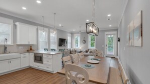 A modern kitchen with white cabinetry, a wooden dining table, and pendant lighting. - Grayton Beach Vacation House- park your car, hop on a bike, explore! (Santa Rosa Beach)