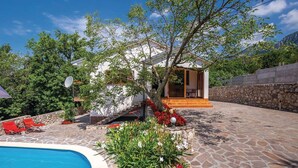 Zona de piscina con patio de piedra, sillas reclinables rojas y un pequeño edificio con balcón.