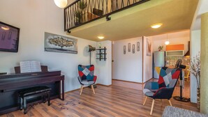 Una sala de estar con un piano, dos sillas coloridas, una estantería y una escalera.