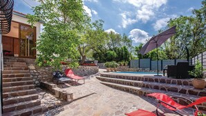 Un patio trasero con un porche de piedra, una piscina y mobiliario exterior.