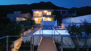 Una casa moderna con piscina, terraza de madera y montañas al fondo.