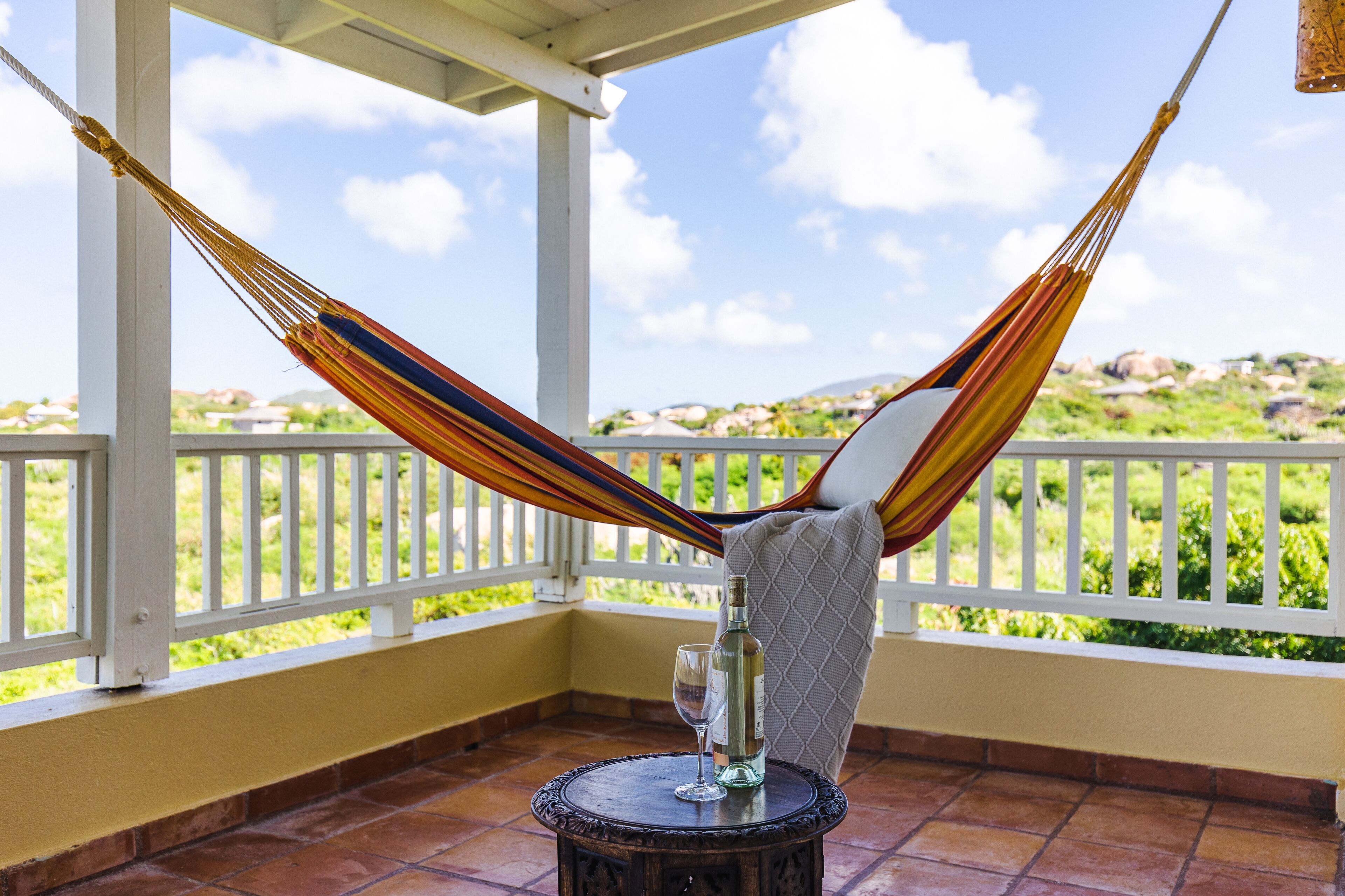 A hammock on a balcony with a table and a bottle.