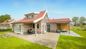 A two-story house with a red-tiled roof, a covered patio with a sofa, and a brick exterior. - Buitengoed het Lageveld - 93 (Hoge Hexel)