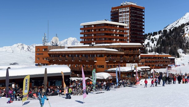 A ski resort with a large building featuring multiple balconies and a ski lift in the background.