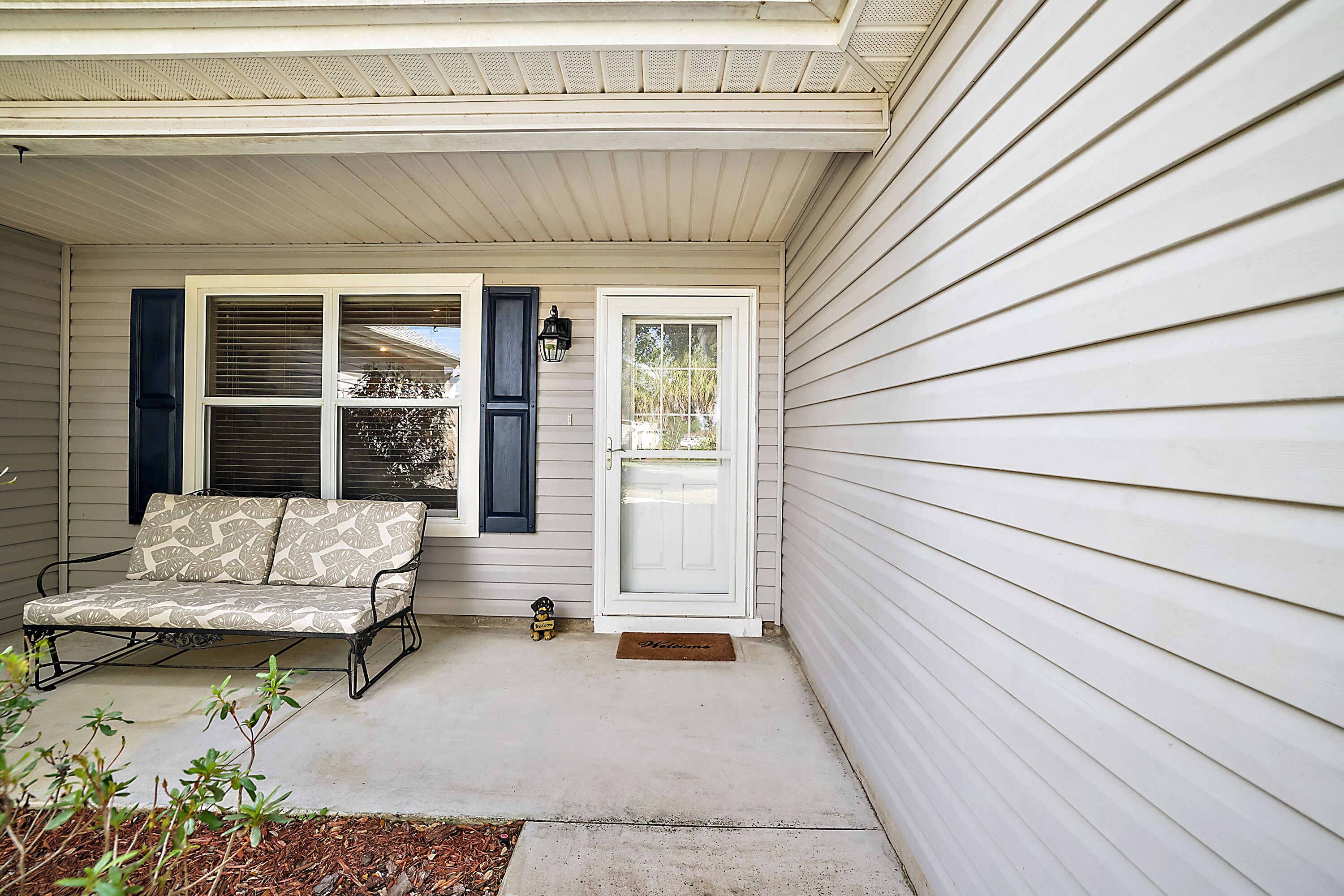 A porch with a bench, a door, and a small dog.