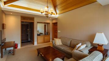 A spacious living room with a high ceiling, a wooden ceiling, a chandelier, a sofa set, a coffee table, a lamp, and a fire extinguisher.