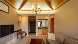 A living room with a wooden ceiling, a chandelier, a television, a bench, a sofa, and a fireplace. - Damyang Hotel (Damyang)