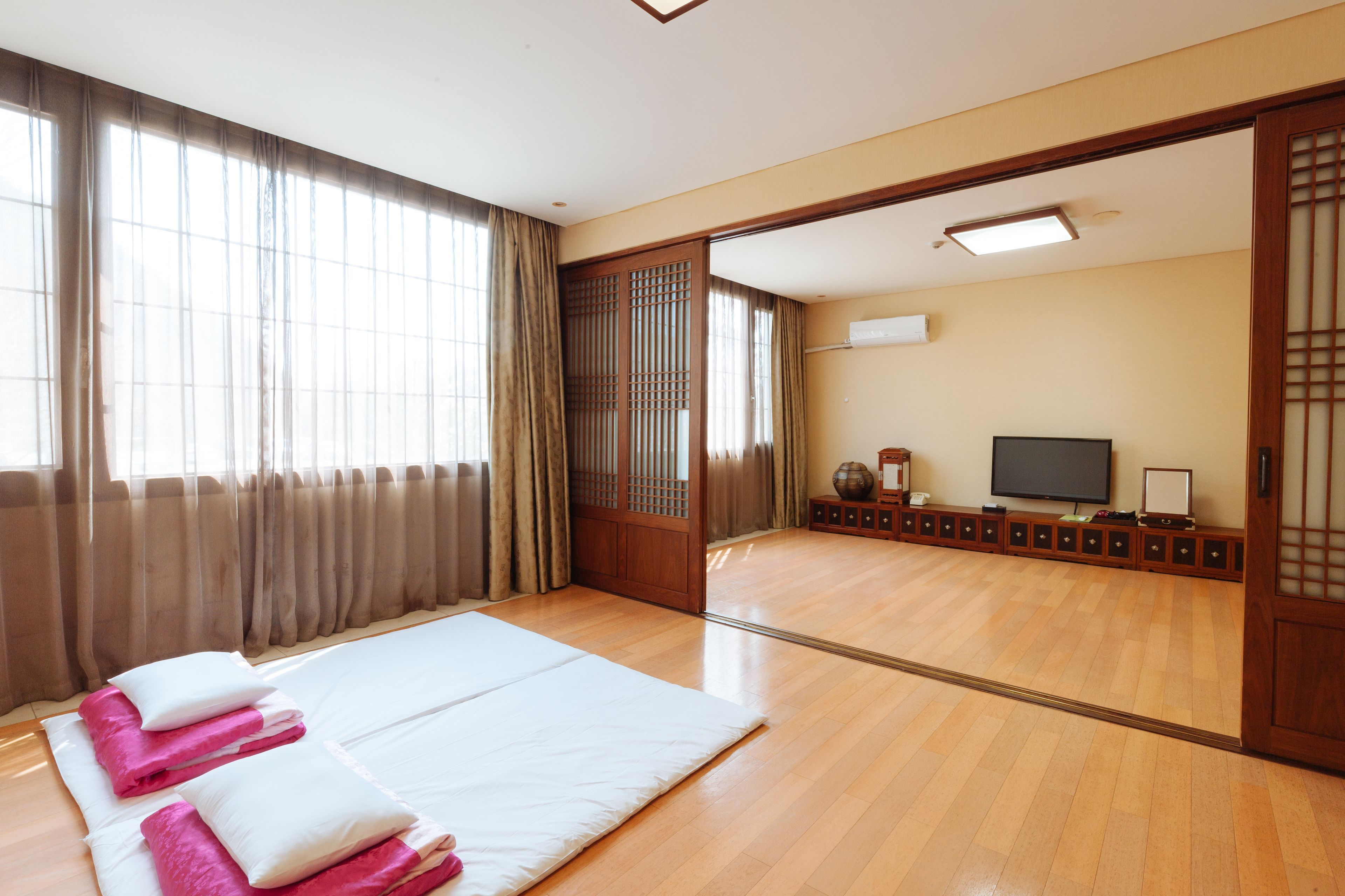 A traditional Japanese-style room with tatami flooring, a large bed with white and pink bedding, a television, and sliding doors.