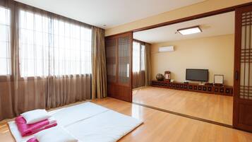 A traditional Japanese-style room with tatami flooring, a large bed with white and pink bedding, a television, and sliding doors.