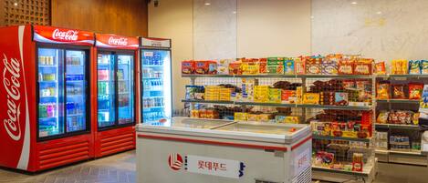 Zona de exhibición refrigerada con enfriadores de Coca-Cola y un congelador, rodeada de estantes llenos de diversos productos envasados.