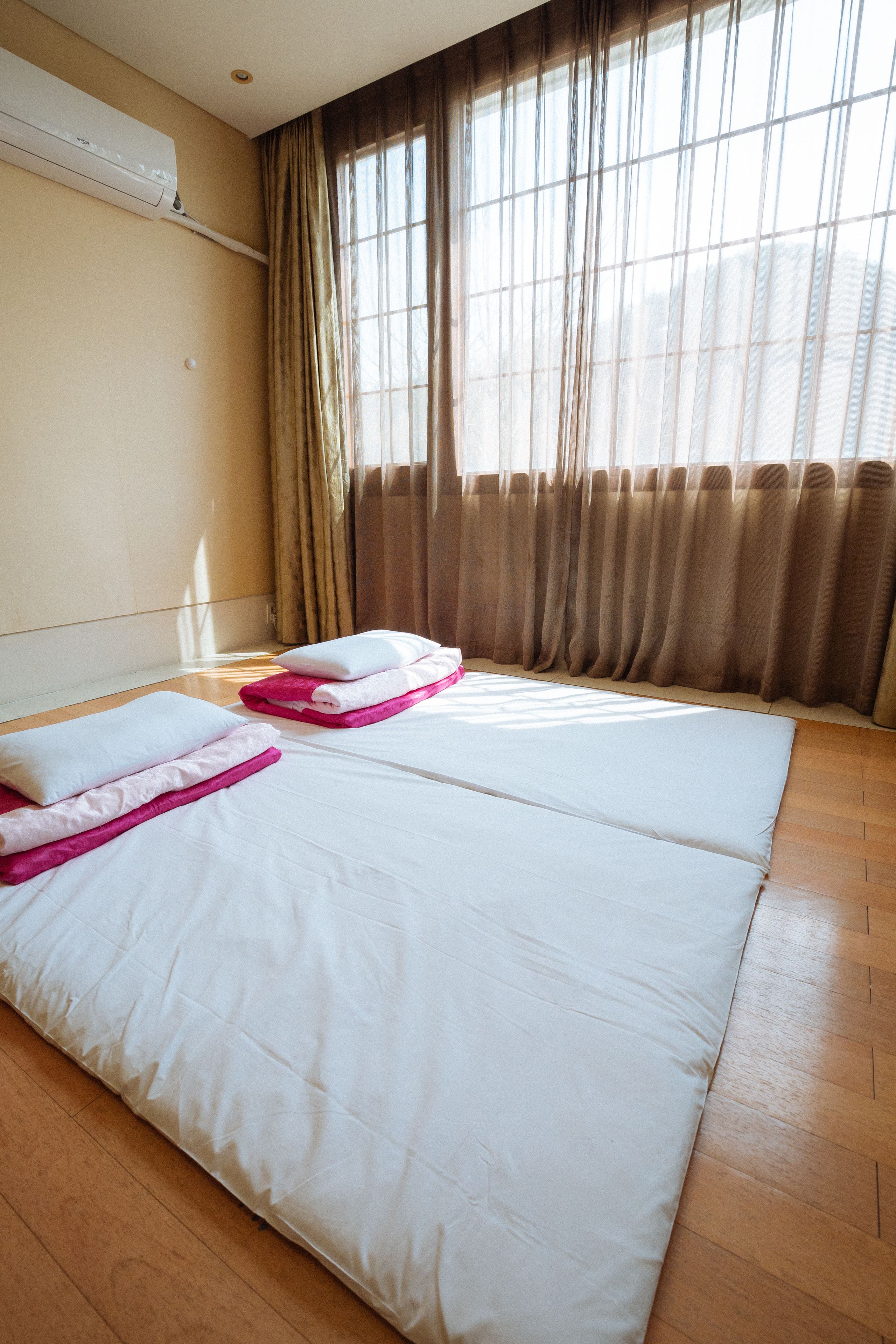 Una habitación de hotel con dos camas, paredes color beige, una ventana con cortinas y un equipo de aire acondicionado.