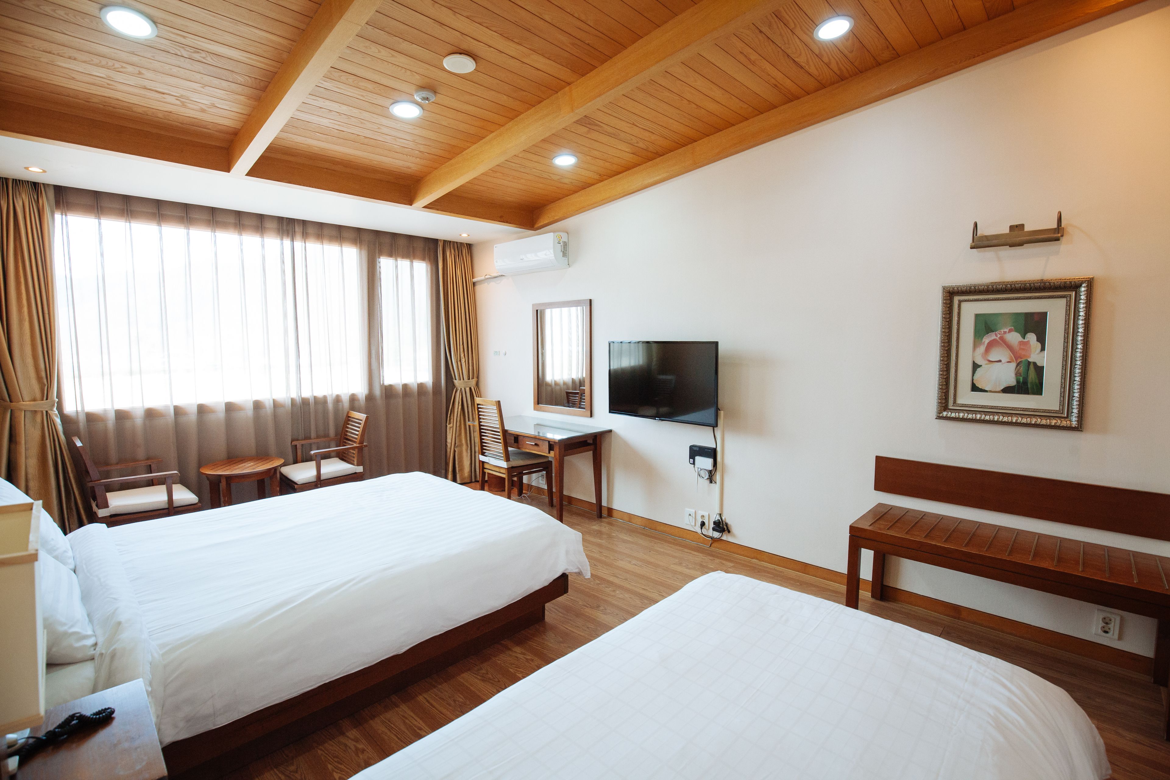 A hotel room with two beds, a desk, a chair, a TV, and a bench.