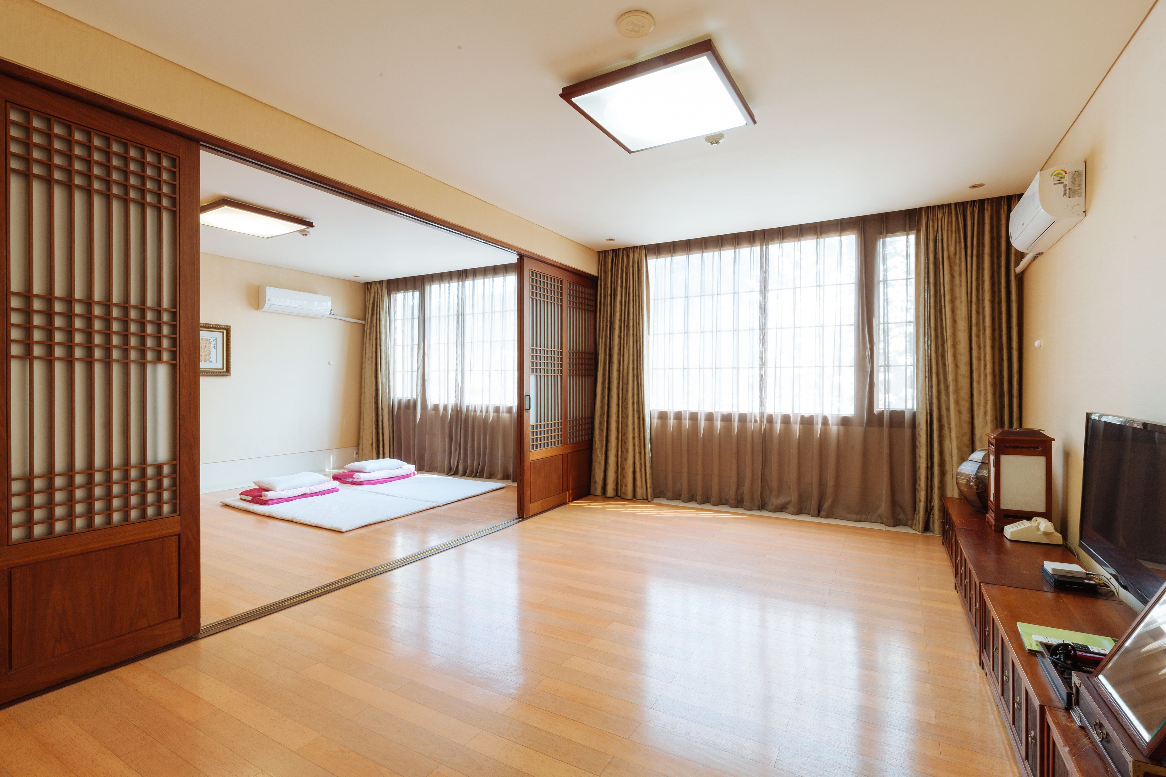 Une pièce spacieuse dotée d’un plancher en bois, d’une porte coulissante, d’un tatami, d’un téléviseur et d’un paravent japonais traditionnel.