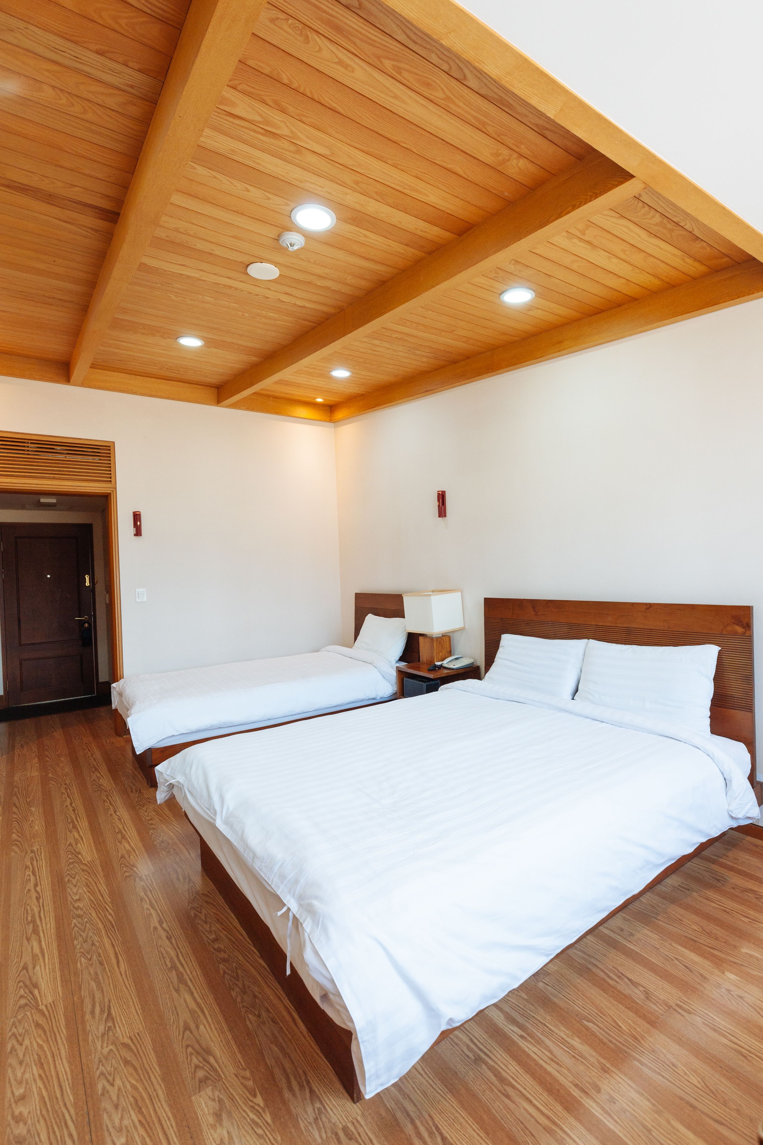 Une chambre d’hôtel avec deux lits, des poutres apparentes en bois au plafond et un éclairage encastré.