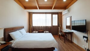 A hotel room with a wooden ceiling, a bed, a desk, a chair, a television, and an air conditioning unit. - Damyang Hotel (Damyang)