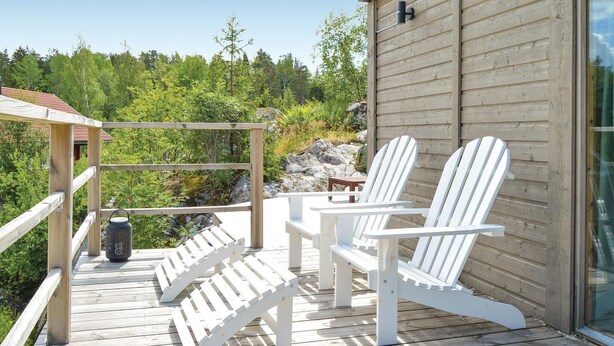 Een houten terras met witte Adirondack-stoelen, een tafeltje en een lantaarn.