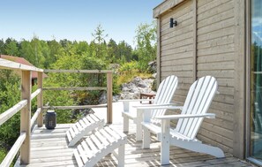 Une terrasse en bois avec des fauteuils Adirondack blancs, une petite table et une lanterne.