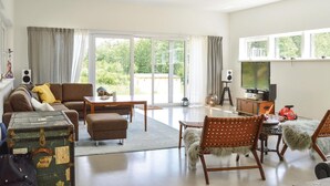 Een woonkamer met een bank, een voetenbankje en een hond. Er is een televisie, speakers en een koffer.