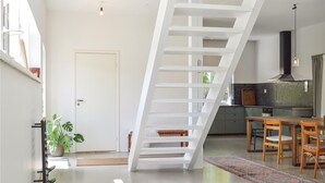 Een modern interieur met een witte trap, een keuken met donkere spatwand en een eetgedeelte met houten meubilair.