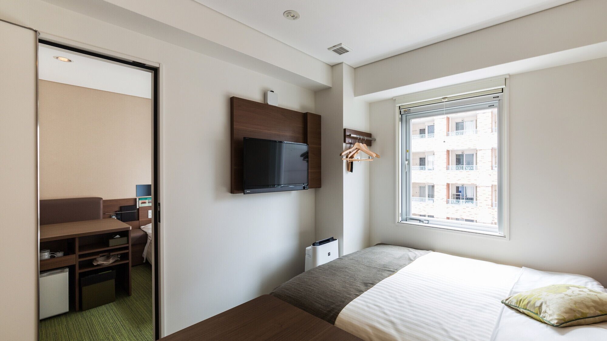 A hotel room with a bed, a desk, a television, and a window with a view of buildings.