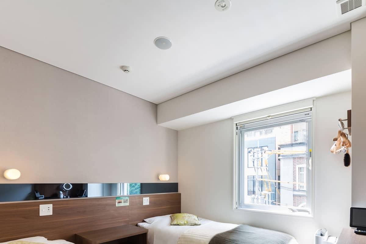 Ein Hotelzimmer mit zwei Betten, einem Schreibtisch, einem Spiegel und einem Fenster mit Blick auf die Stadt.