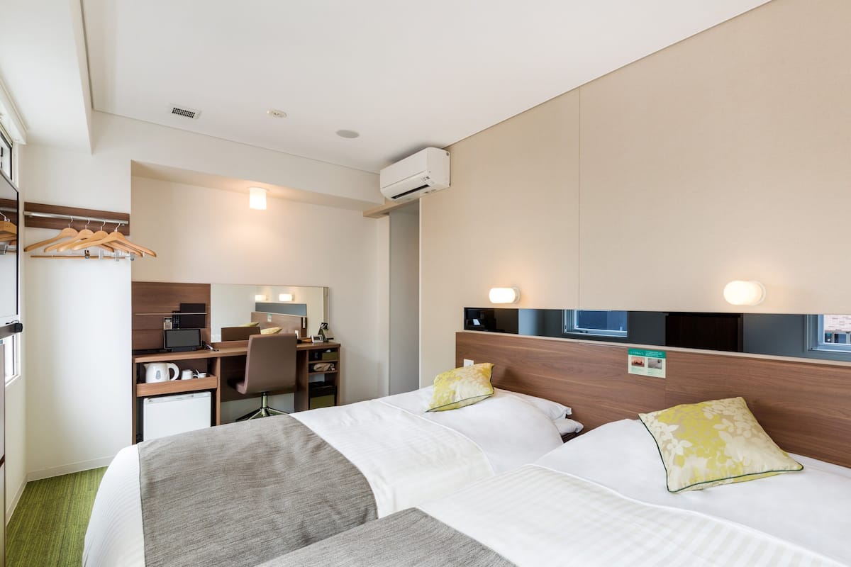 Ein Hotelzimmer mit zwei Betten, einem Schreibtisch mit Stuhl, einer Mikrowelle und einer kleinen Küchenzeile.