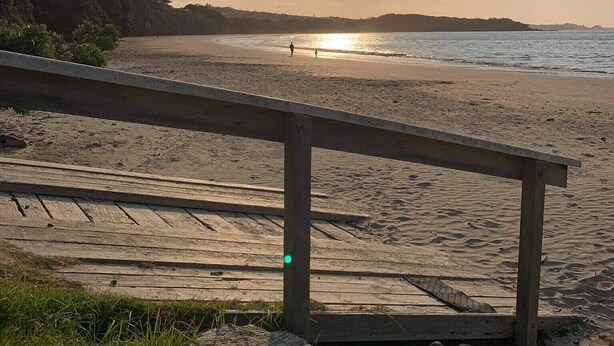 Une plage avec une promenade en bois menant à l’eau, un ciel dégagé et le soleil se couchant ou se levant.