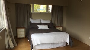 Une chambre avec un grand lit, deux tables de chevet, une fenêtre avec des rideaux et un plancher en bois.