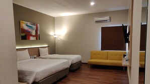 A hotel room with two beds, a sofa, a painting, an air conditioning unit, and a wooden floor. - Havana Mutiara Belitung Hotel (Tanjung Pandan)