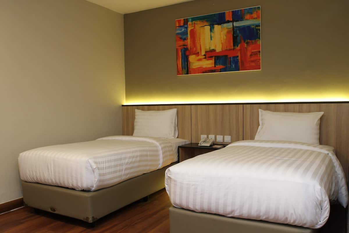 A hotel room with two beds, a wooden headboard, a painting on the wall, and a bedside table with a phone.
