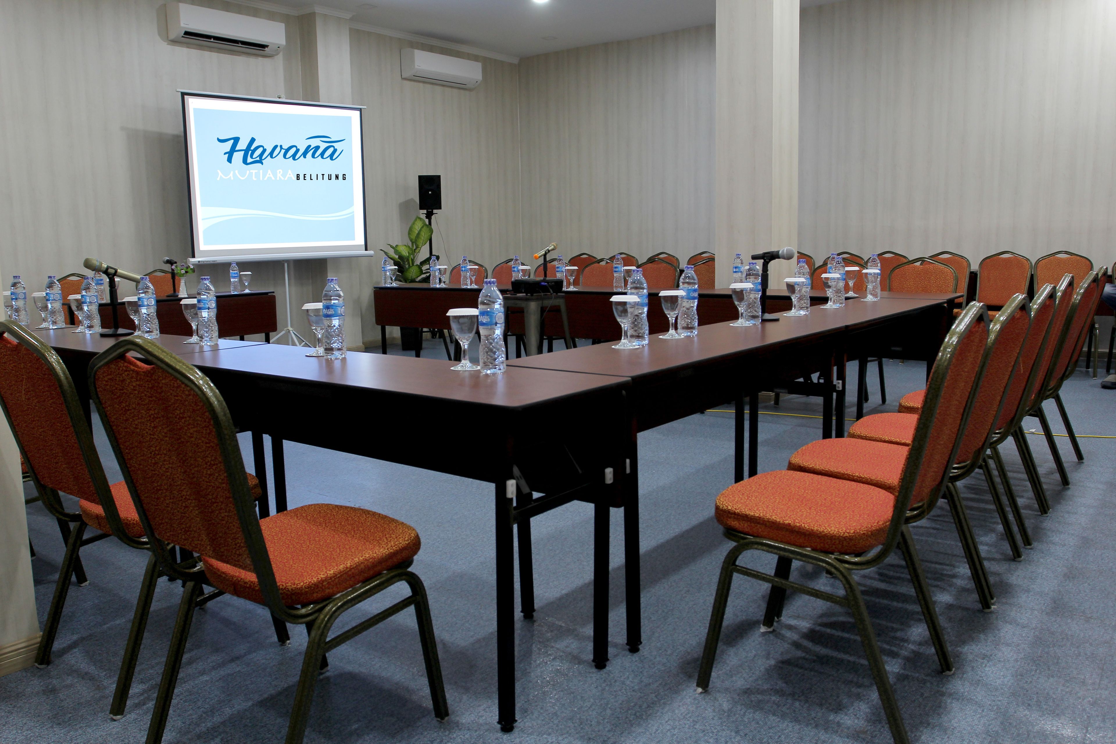 Een vergaderruimte met een lange tafel, stoelen, waterflesjes en een scherm waarop 'Havana' staat.
