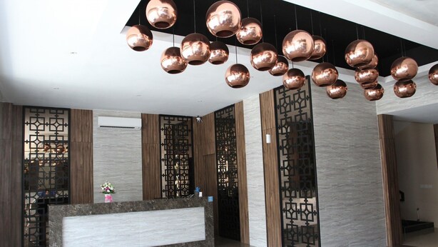A reception area with a marble reception desk, decorative metal wall panels, and a modern chandelier. - Havana Mutiara Belitung Hotel (Tanjung Pandan)