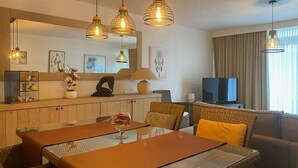 A modern living room with a dining area, featuring a large mirror, hanging pendant lights, and a television. - Astrid 103 with balcony by Interhome (Bredene)