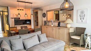 A modern living room with a grey sofa, wicker chairs, a dining area, and a kitchen in the background. - Astrid 103 with balcony by Interhome (Bredene)