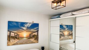 A bedroom with a large wall-mounted picture of a sunset over a beach, a bed, a wardrobe, and a bedside lamp. - Astrid 103 with balcony by Interhome (Bredene)