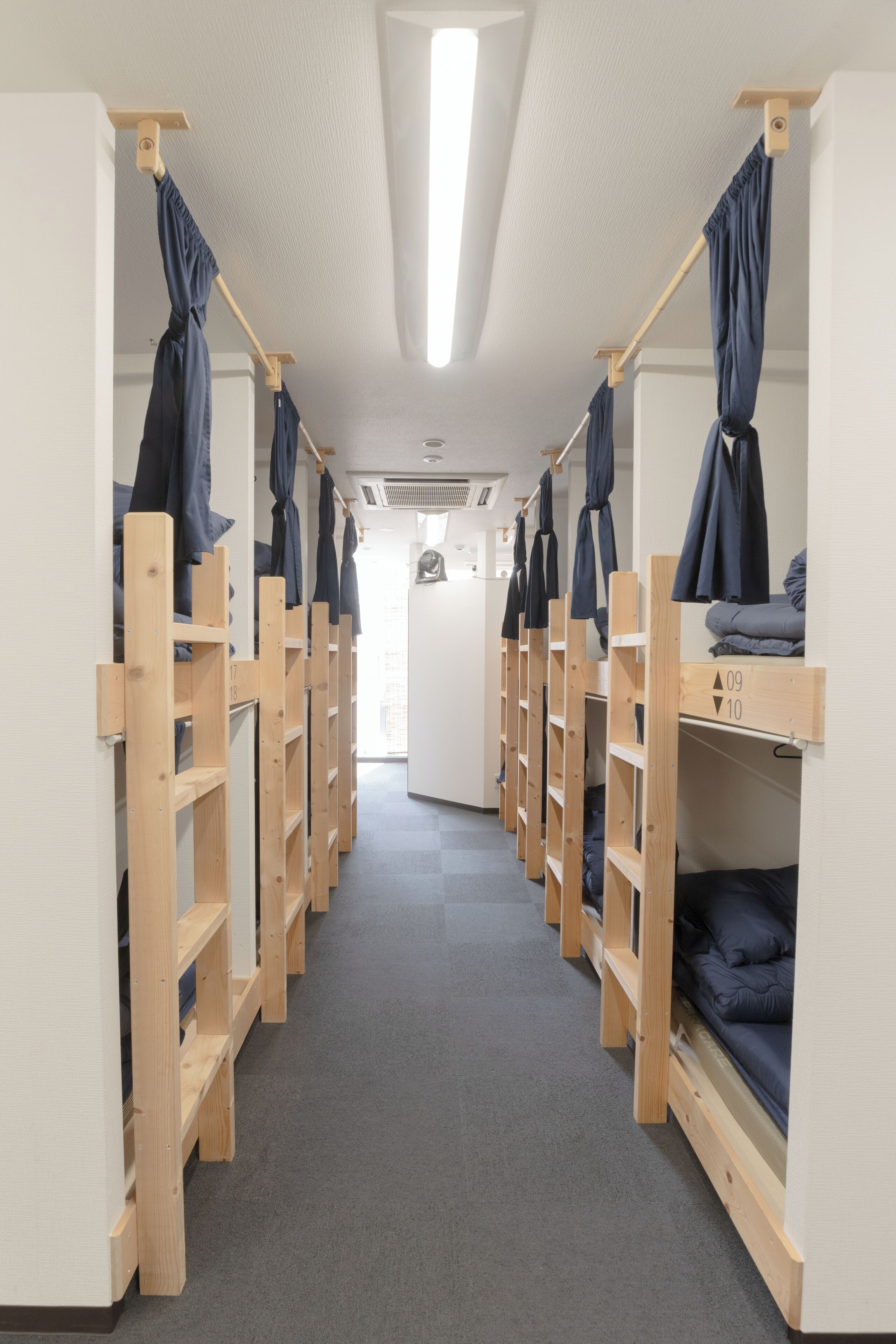 A corridor with bunk beds, each with a wooden frame and a hanging garment.