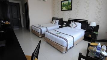 A hotel room with two single beds, a desk, a chair, a TV, and a small table with a lamp and a bottle.