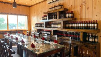 A restaurant interior with a long dining table set for multiple guests, wooden walls, and a wine rack filled with bottles.